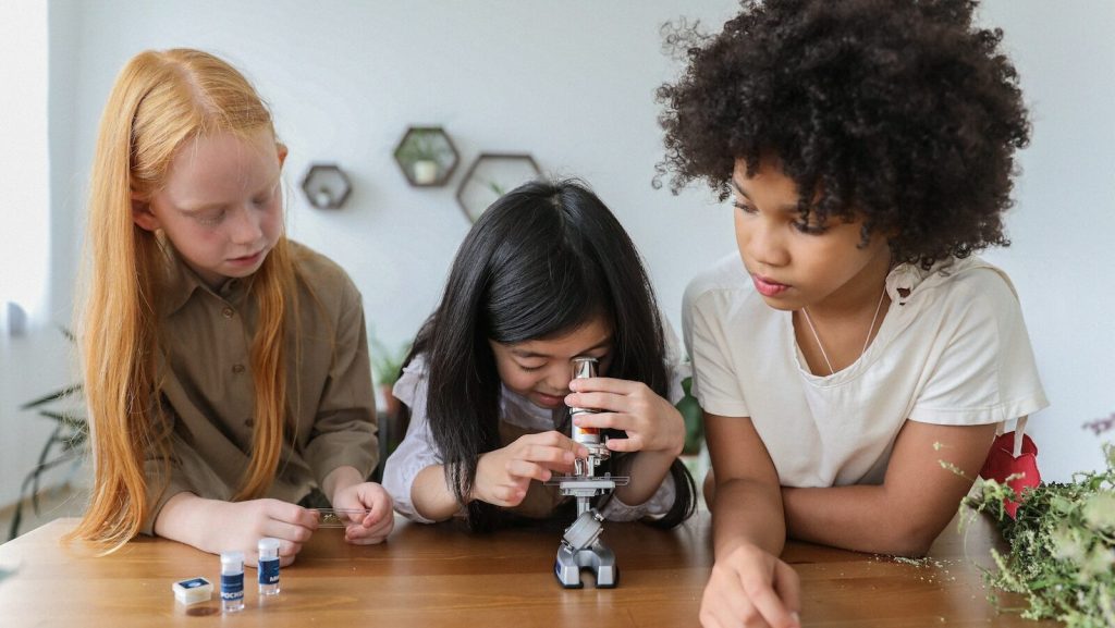 Concentrated multiethnic children in casual clothes watching in microscope while studying together
