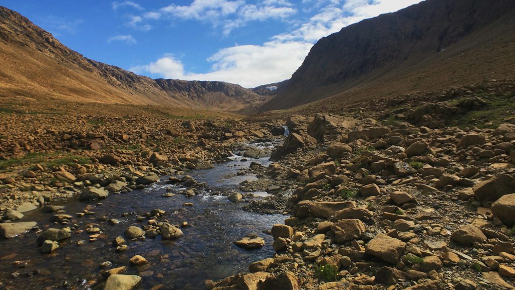 a rocky river running through a valley surrounded by mountains